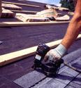 An adult male is using the tool as described to shingle a roof.