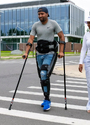 A man walking along a pedestrian crossing wearing an Ekso Indego Mobility Exoskeleton and using crutches.